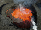Pohled na lávové jezero v jícnu sopky Sundhnúkur na poloostrově Reykjanes během erupce v dubnu 2024. Je zde patrná tmavá zvlněná svrchní krusta chladnoucí lávy a neklidná hladina vyvrhující žhavou hmotu do výšky a do stran. Lávová hmota letící vzduchem pak může ze strany připomínat fontánu nebo oheň. Jako ohně nazývali erupce v této oblasti obyvatelé Islandu při posledních erupcích ve 13. století. Na levé straně je vidět proud lávy vytékající z jezera. Teplota lávy zde přesahovala 1 100 °C. Foto J. Klicpera, Geofyzikální ústav AV ČR
